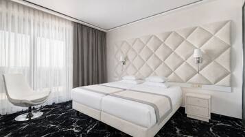 Habitación de hotel moderna con una cama grande, una silla, una mesita de noche y suelo de mármol.