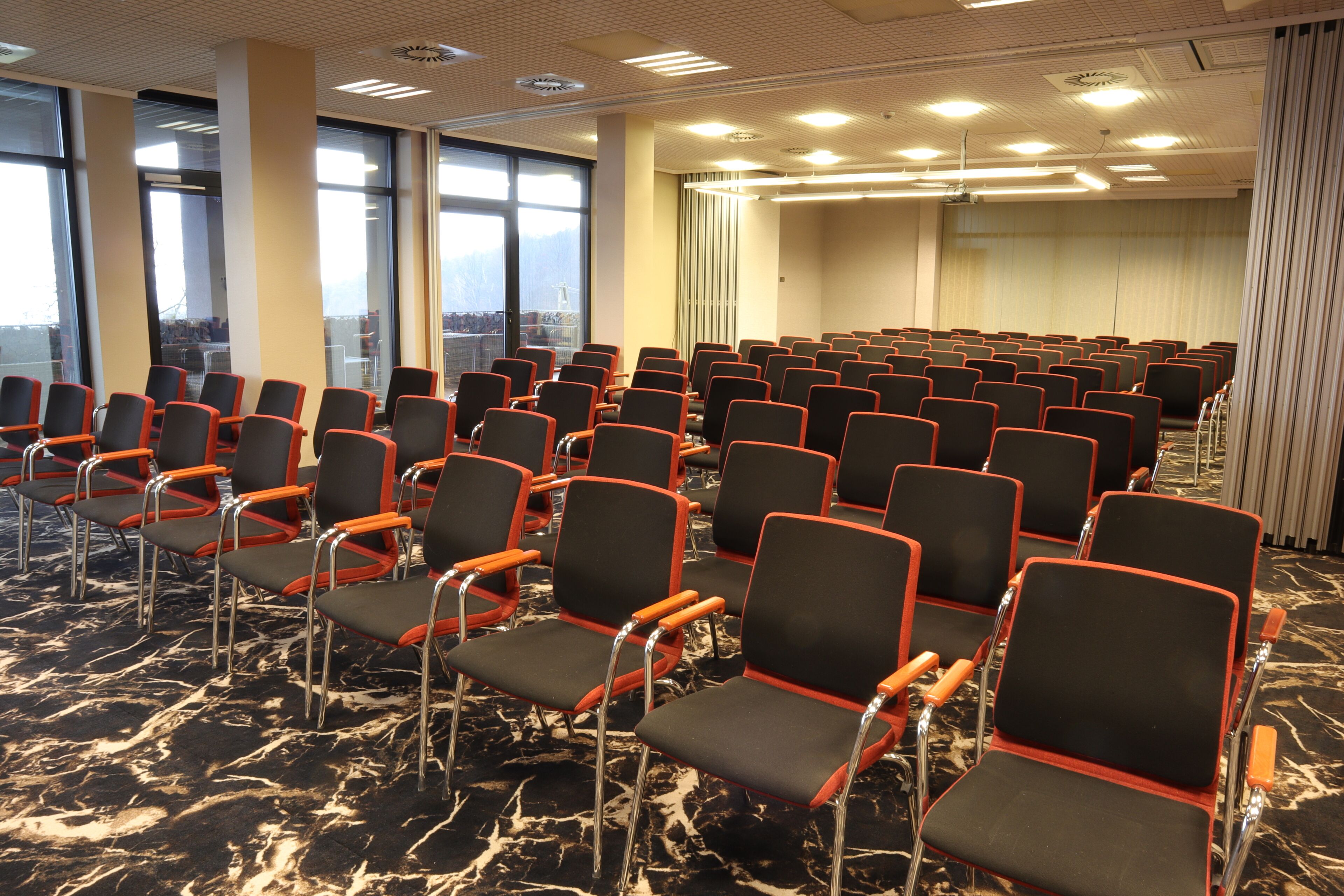 A conference room with rows of black chairs with red accents, large windows, and a marble floor.