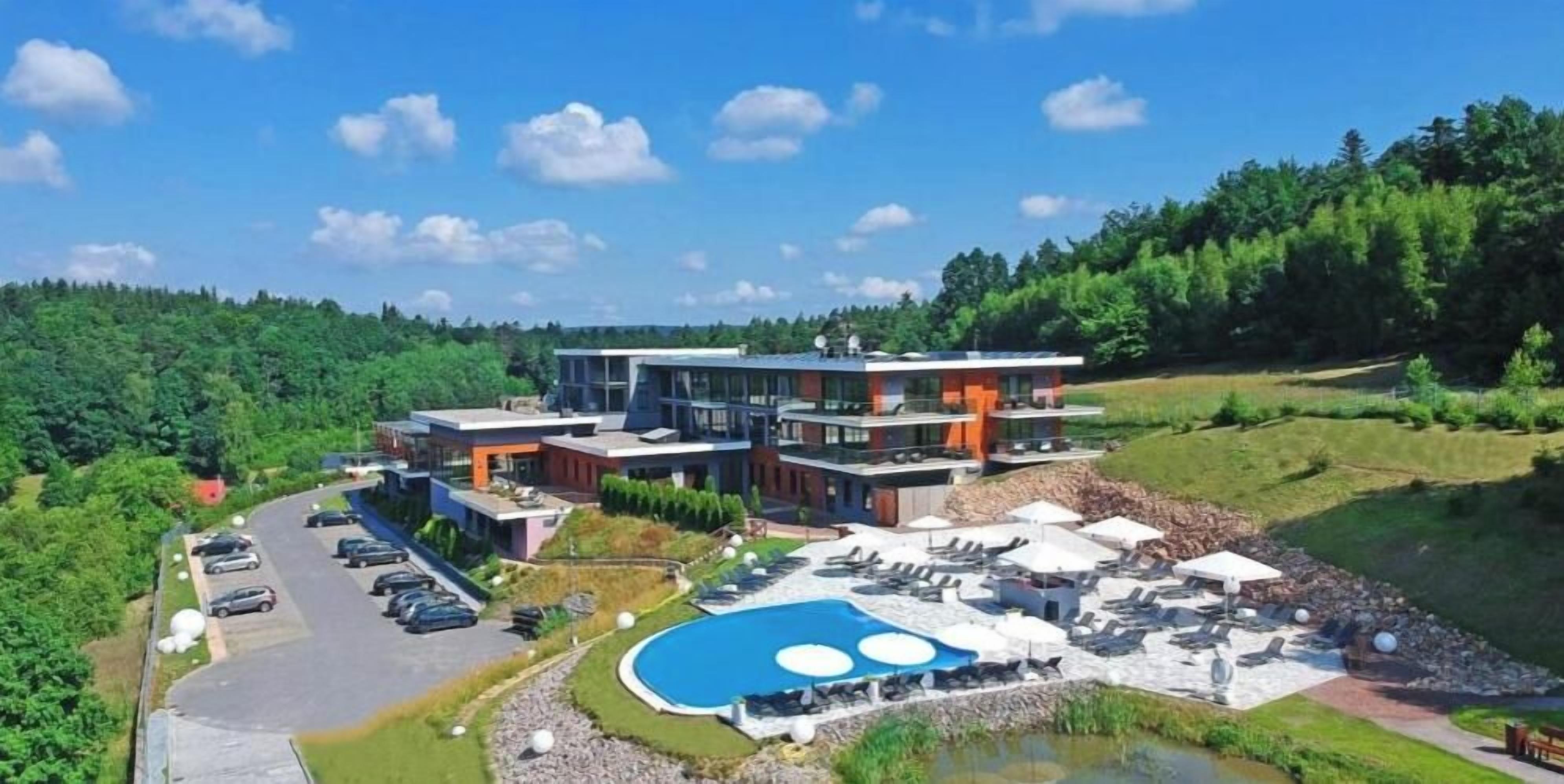 A modern hotel with a swimming pool, outdoor seating, and a parking area.
