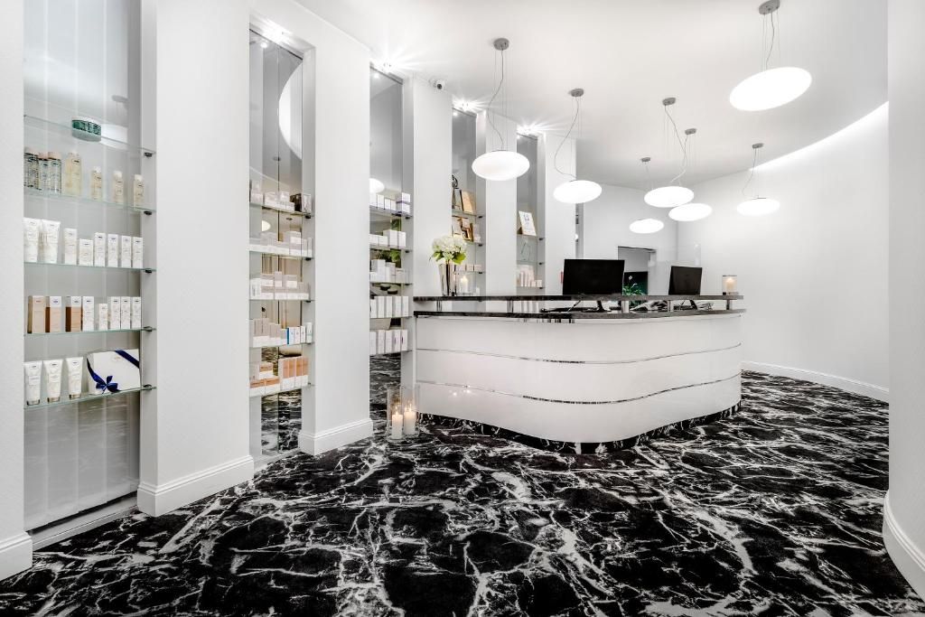 A modern reception area with a marble floor, white reception desk, and shelves with products.