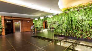 A modern lobby with a reception desk, a glass railing, and a vertical garden wall. - Odyssey ClubHotel Wellness & SPA (Maslów)