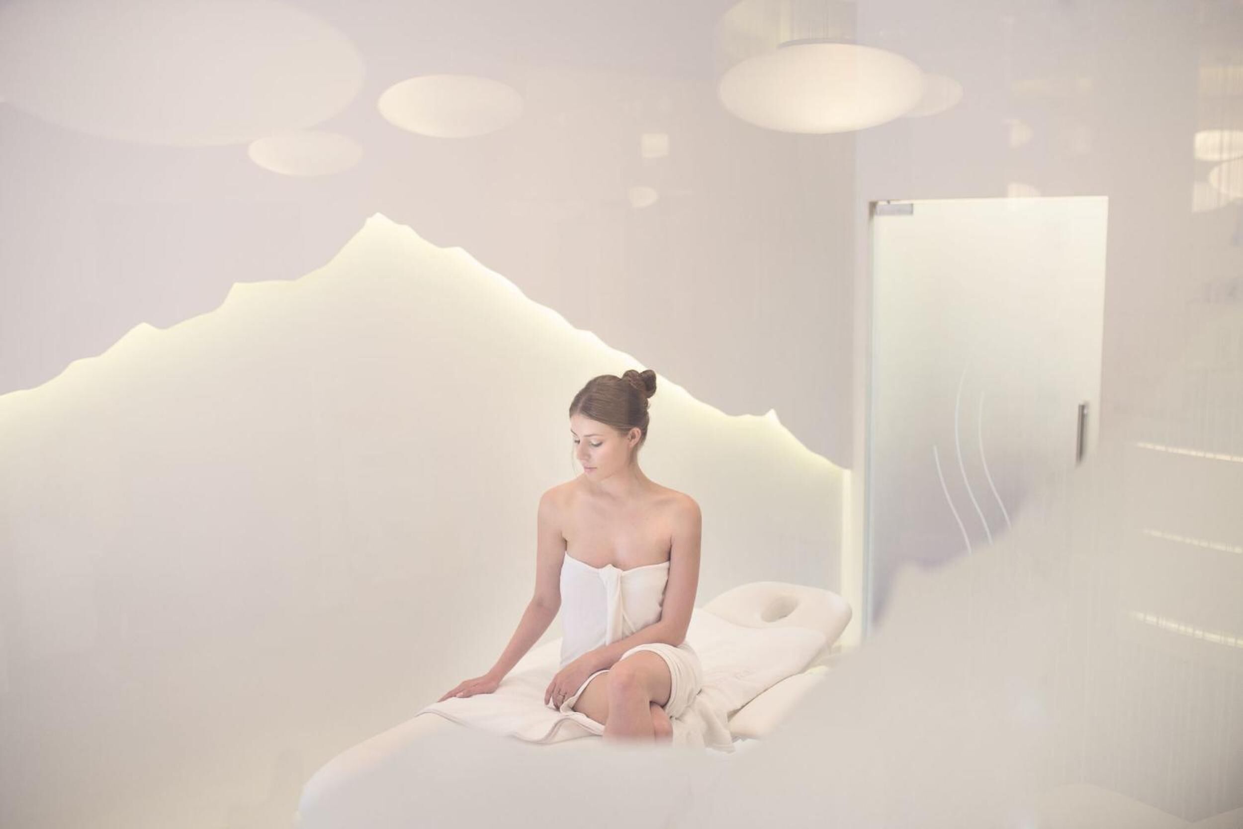 Une salle de spa avec un mur blanc dont le décor évoque une montagne, un lit et une porte.