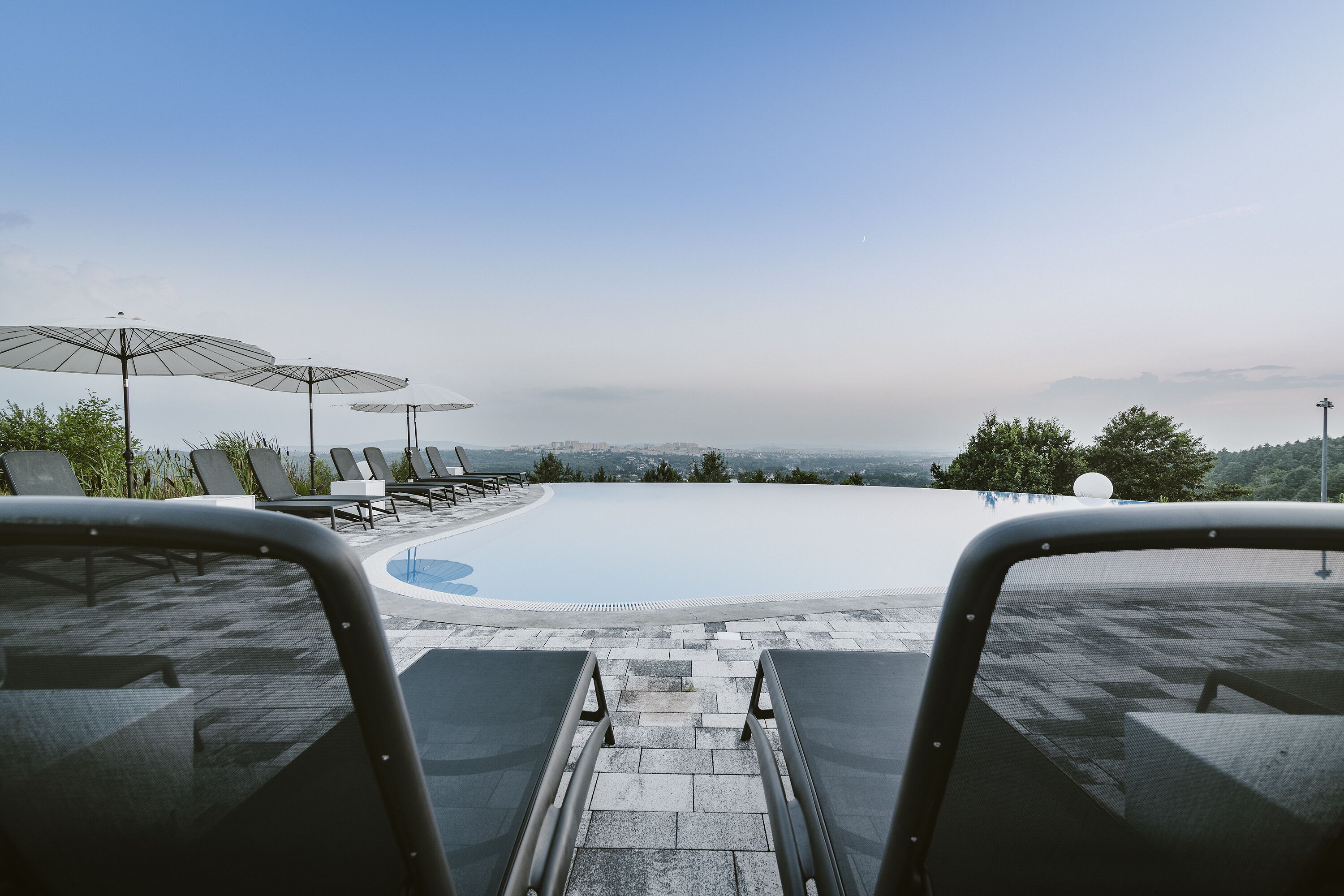 A pool area with lounge chairs and umbrellas, a clear view of the landscape, and a stone pathway leading to the pool.