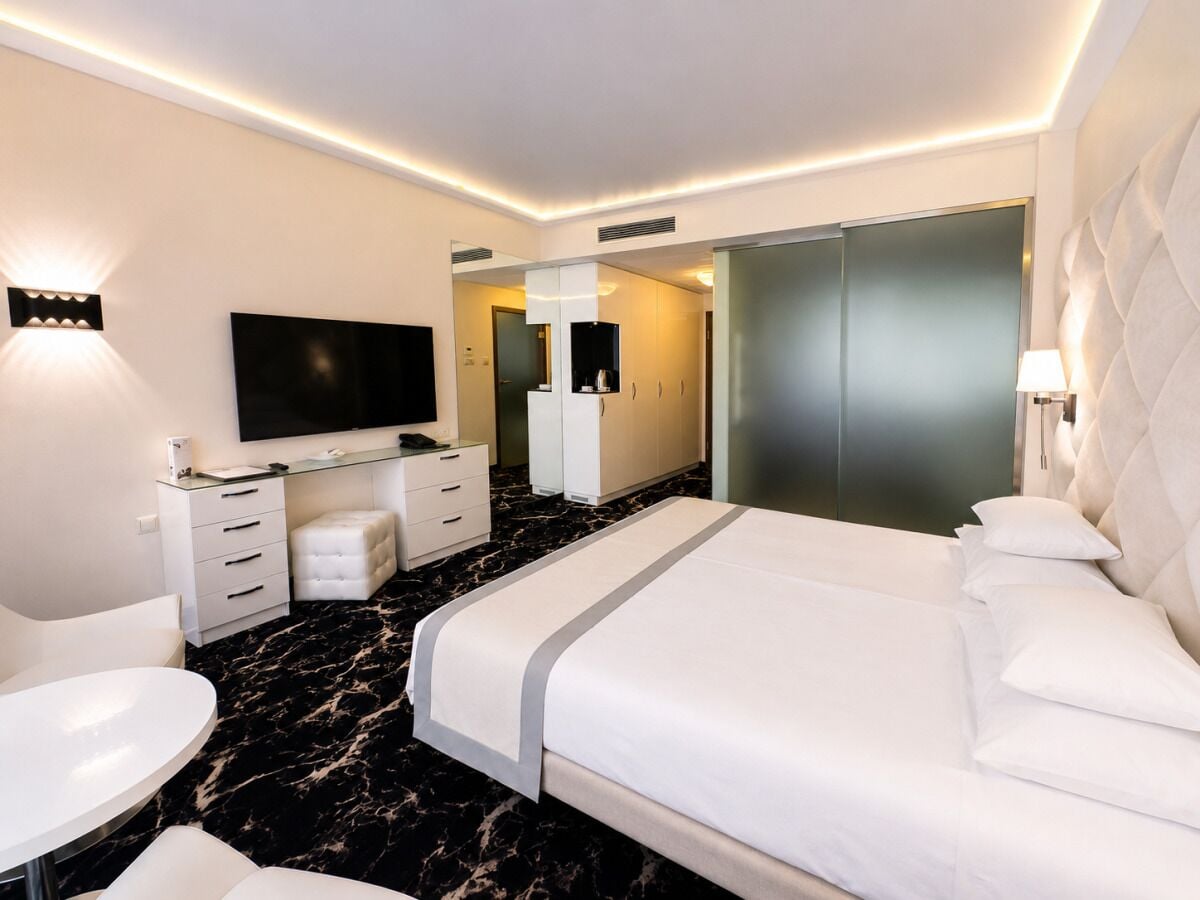 A modern hotel room with a large bed, a desk, a flat-screen TV, and a seating area.