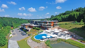A modern hotel with a swimming pool, outdoor seating, and a parking lot. - Odyssey ClubHotel Wellness & SPA (Maslów)