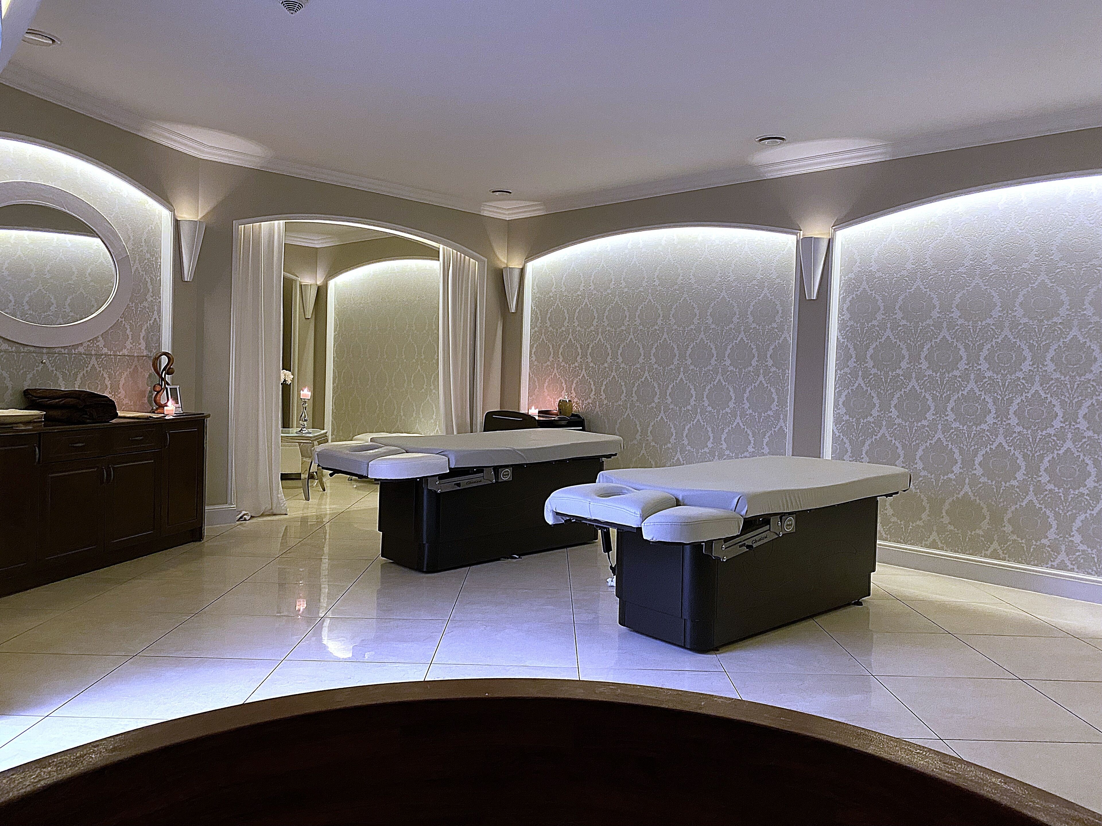 A spa room with two massage tables, a vanity with a mirror, and a large mirror on the wall.