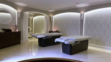 A spa room with two massage tables, a vanity with a mirror, and a large mirror on the wall.