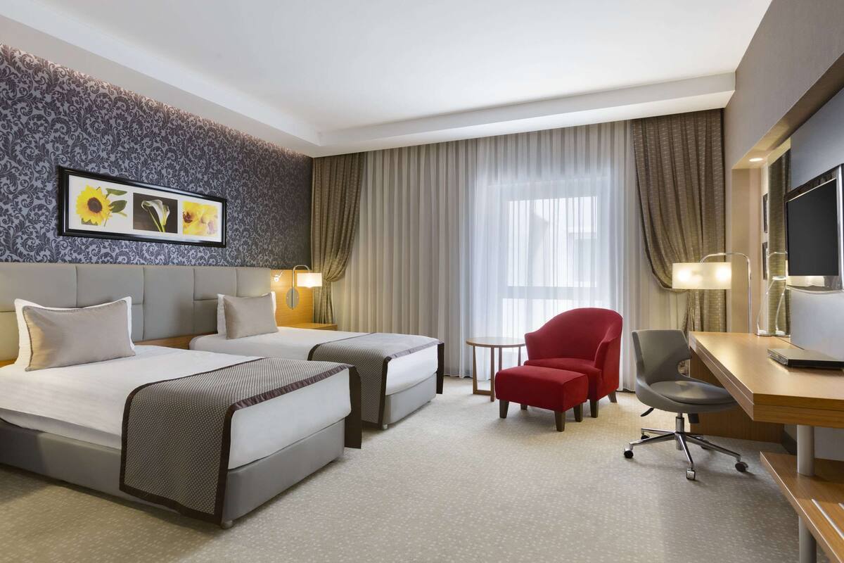 Habitación de hotel con dos camas, un escritorio, una silla, un televisor y una ventana con cortinas.