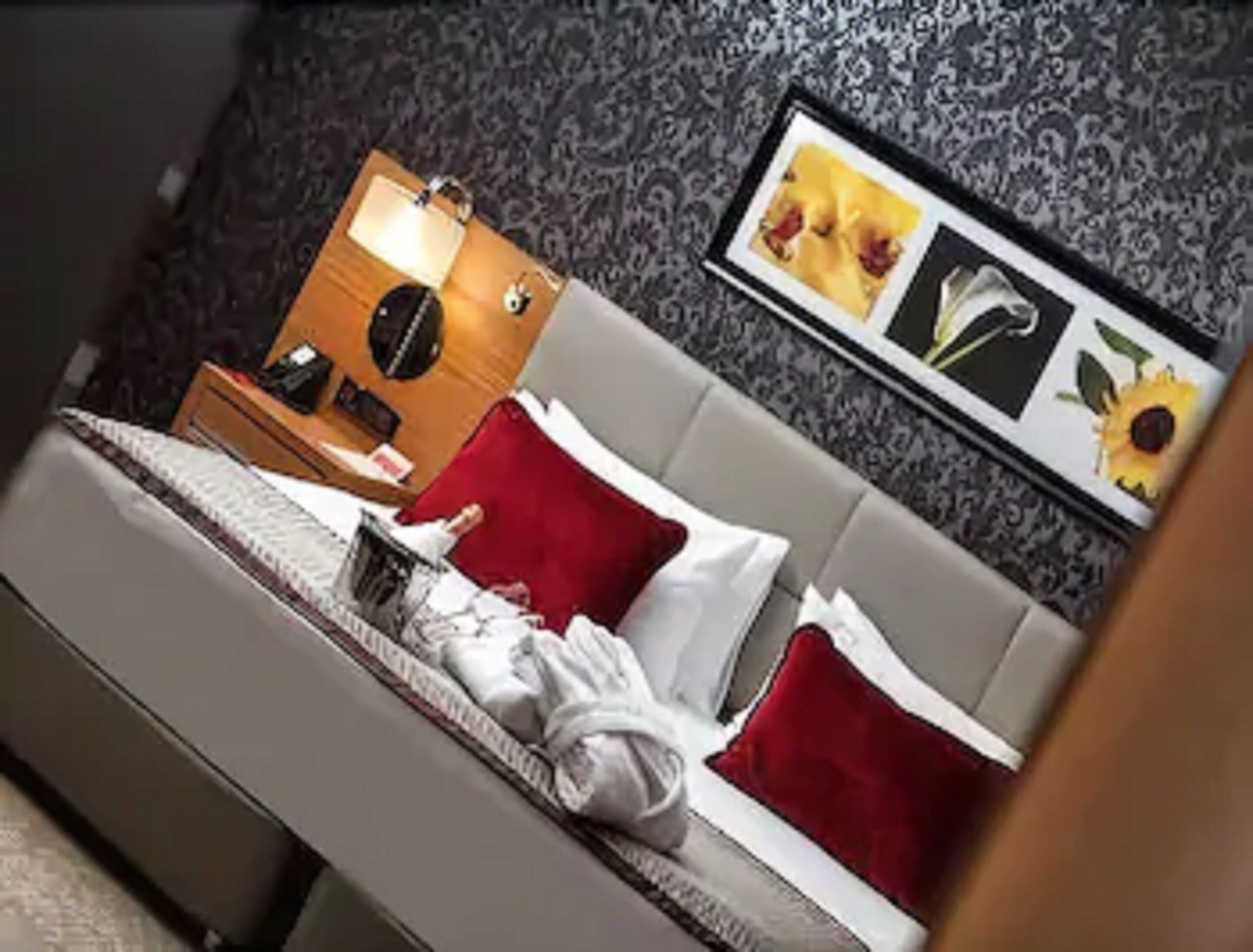 A neatly made bed with red and white pillows, a bedside table with a lamp, and a wall with framed pictures.