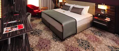 A hotel room with a large bed, a desk, a red chair, and a patterned carpet.