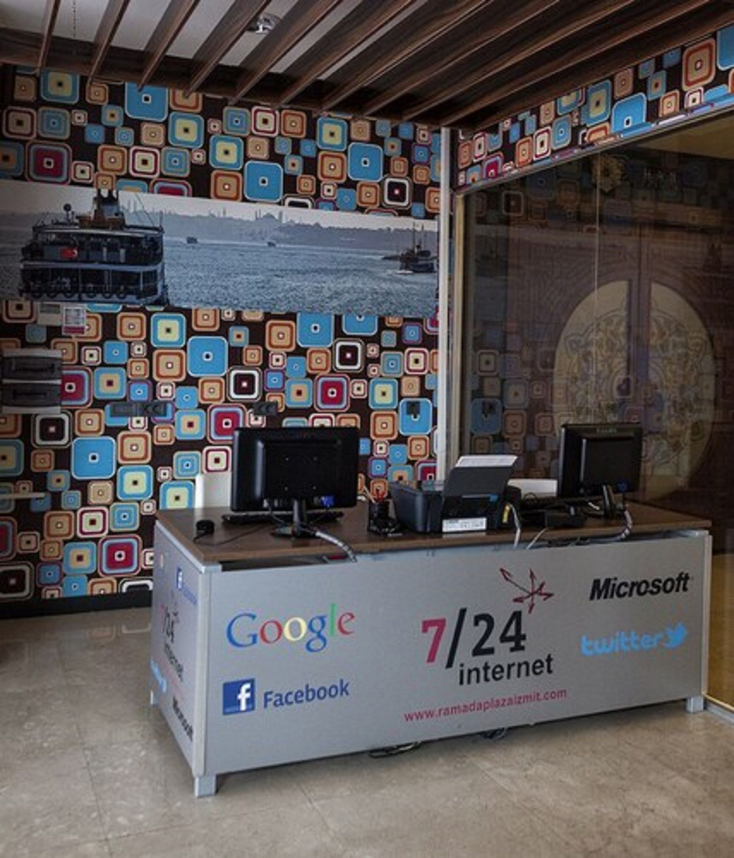 A reception desk with logos of Google, Facebook, Microsoft, and Twitter, and a website address.