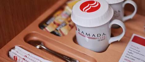 A tray with two white mugs labeled "RAMADA AZEAT PZMIT," a spoon, and several packaged snacks.