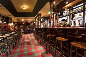A bar area with a checkered floor, wooden bar stools, and a variety of bottles and glasses on shelves.