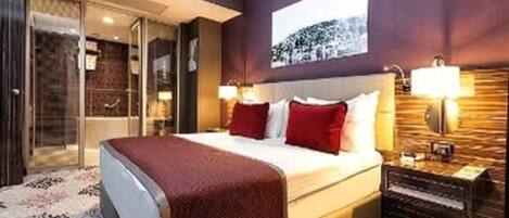 Una habitación de hotel con una cama grande, cabina de ducha de vidrio y cabecero de madera.