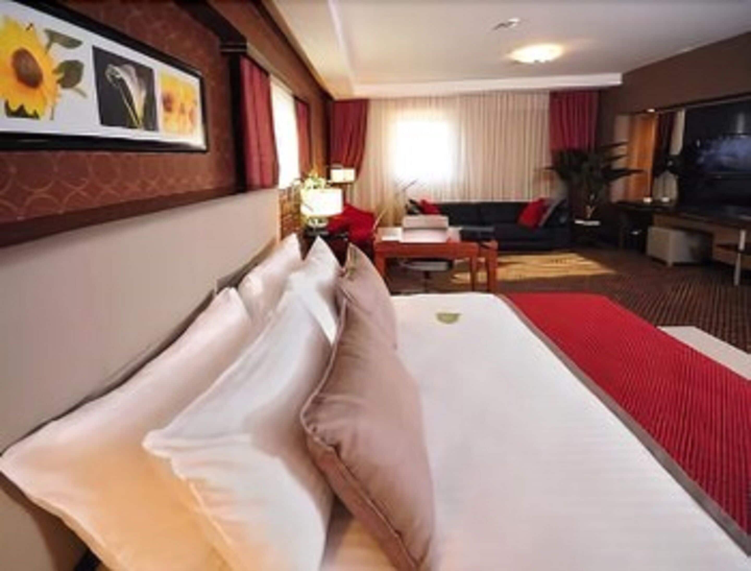 Una habitación de hotel con cama, sofá, televisión y ventana con cortinas.