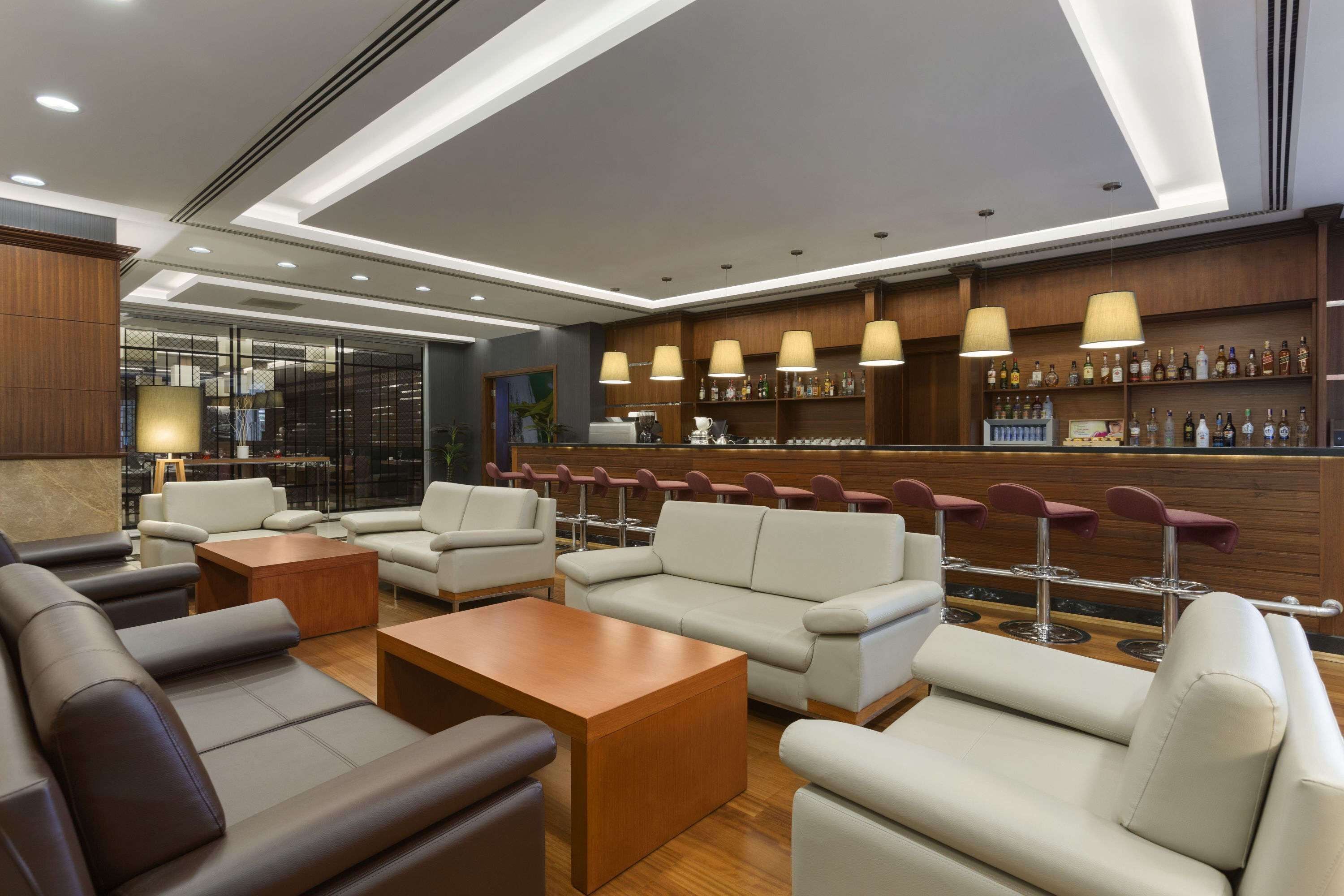 A modern lounge area with leather sofas, wooden coffee tables, and a bar with a variety of liquor bottles.