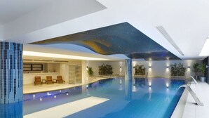Una amplia piscina interior con techo que simula un cielo estrellado, zona de estar con sillas y una fuente de agua.