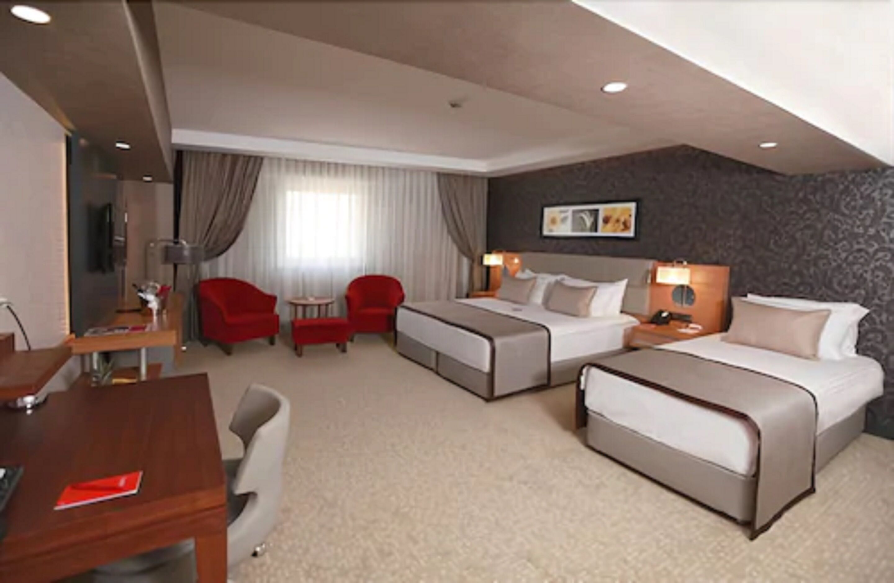 A hotel room with a bed, two armchairs, a desk, and a small table.