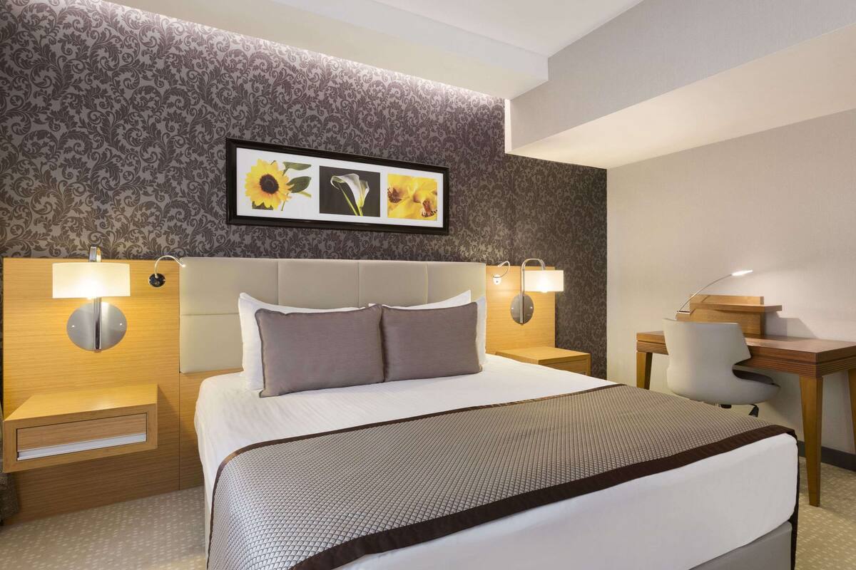 Habitación de hotel con una cama grande, dos mesitas de noche con lámparas, un escritorio de madera y una silla.