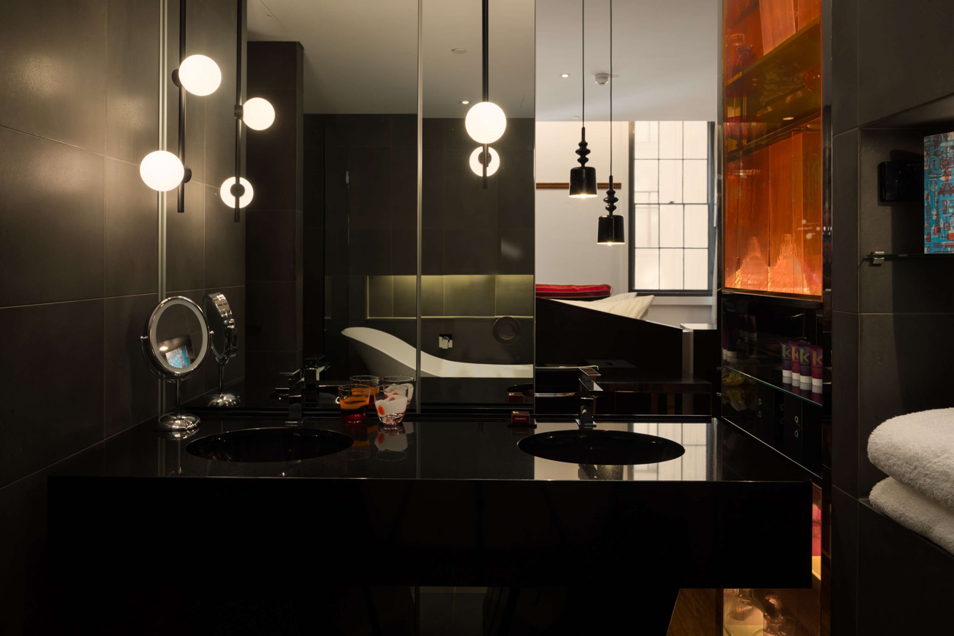 A modern bathroom with a black vanity, a round mirror, and multiple pendant lights.