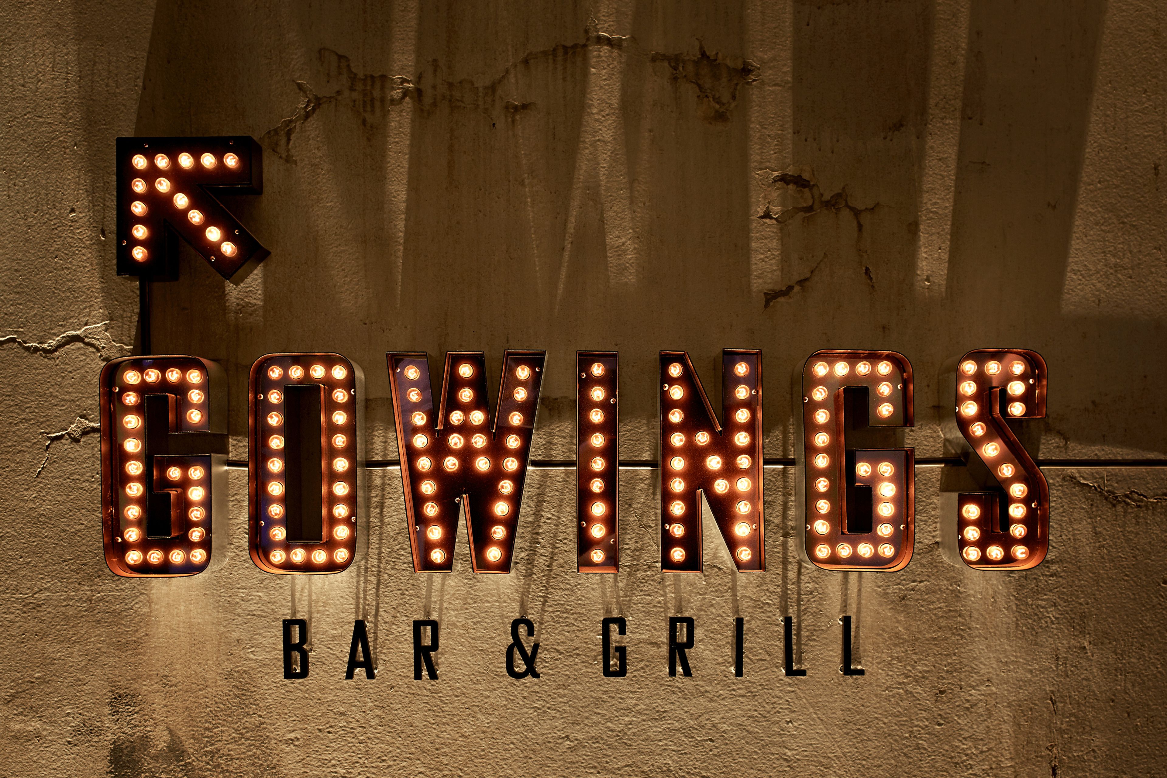Illuminated neon letters spelling "GOWINGS BAR & GRILL" against a textured wall.