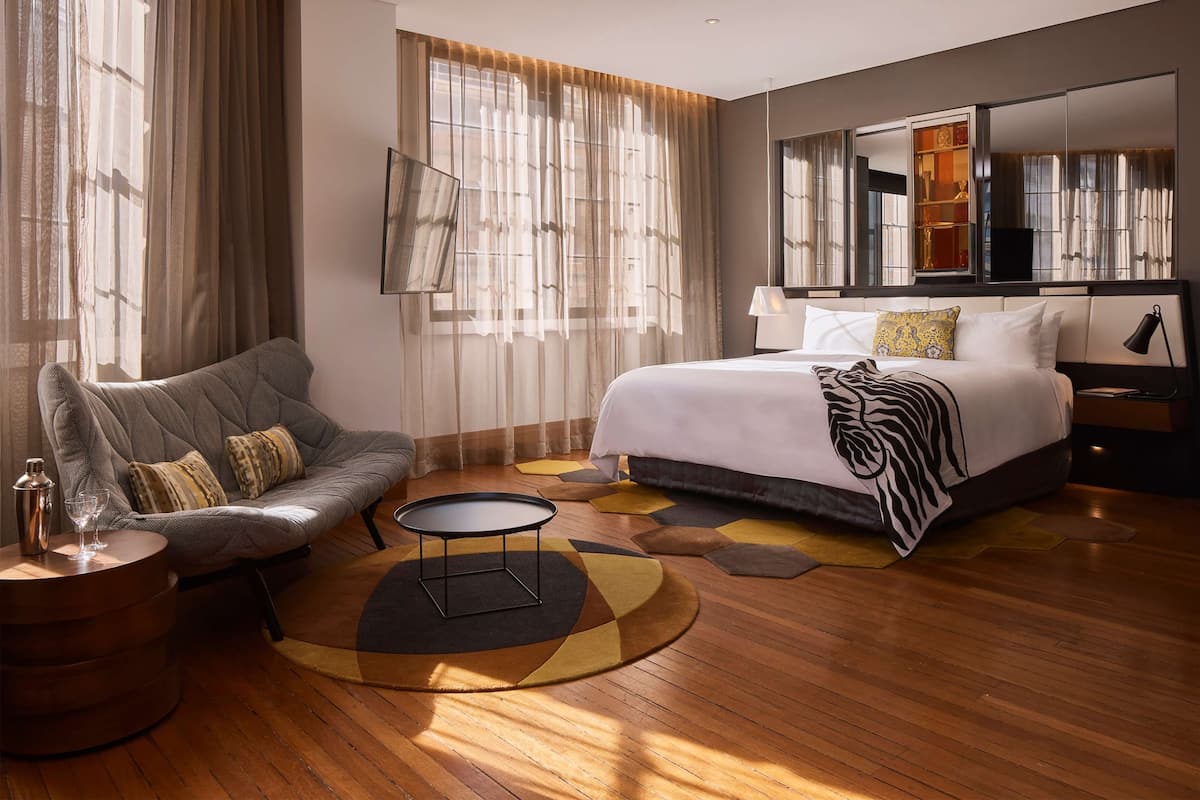 A modern hotel room with a large bed, a sofa, a round coffee table, and a large mirror.