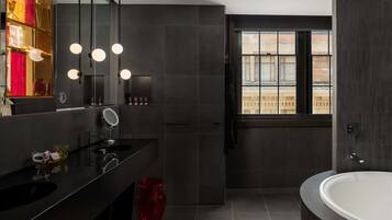 Un baño moderno con baldosas oscuras, un espejo grande, una bañera redonda y una ventana con vistas a edificios.