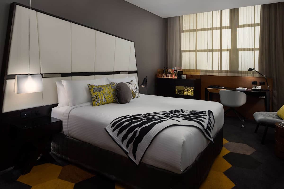 A modern hotel room with a large bed, a desk, and a chair.