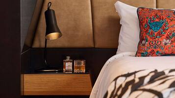Un dormitorio moderno con cabecera de madera, una mesita de noche con lámpara, dos botellas de licor y un cojín estampado.