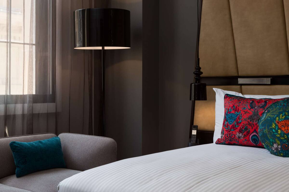 A hotel room with a bed, a sofa, a lamp, and a window with curtains.