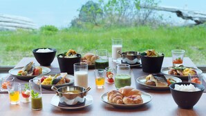 Una mesa servida con diversos platos y bebidas, con vistas a un paisaje de vegetación y una masa de agua.