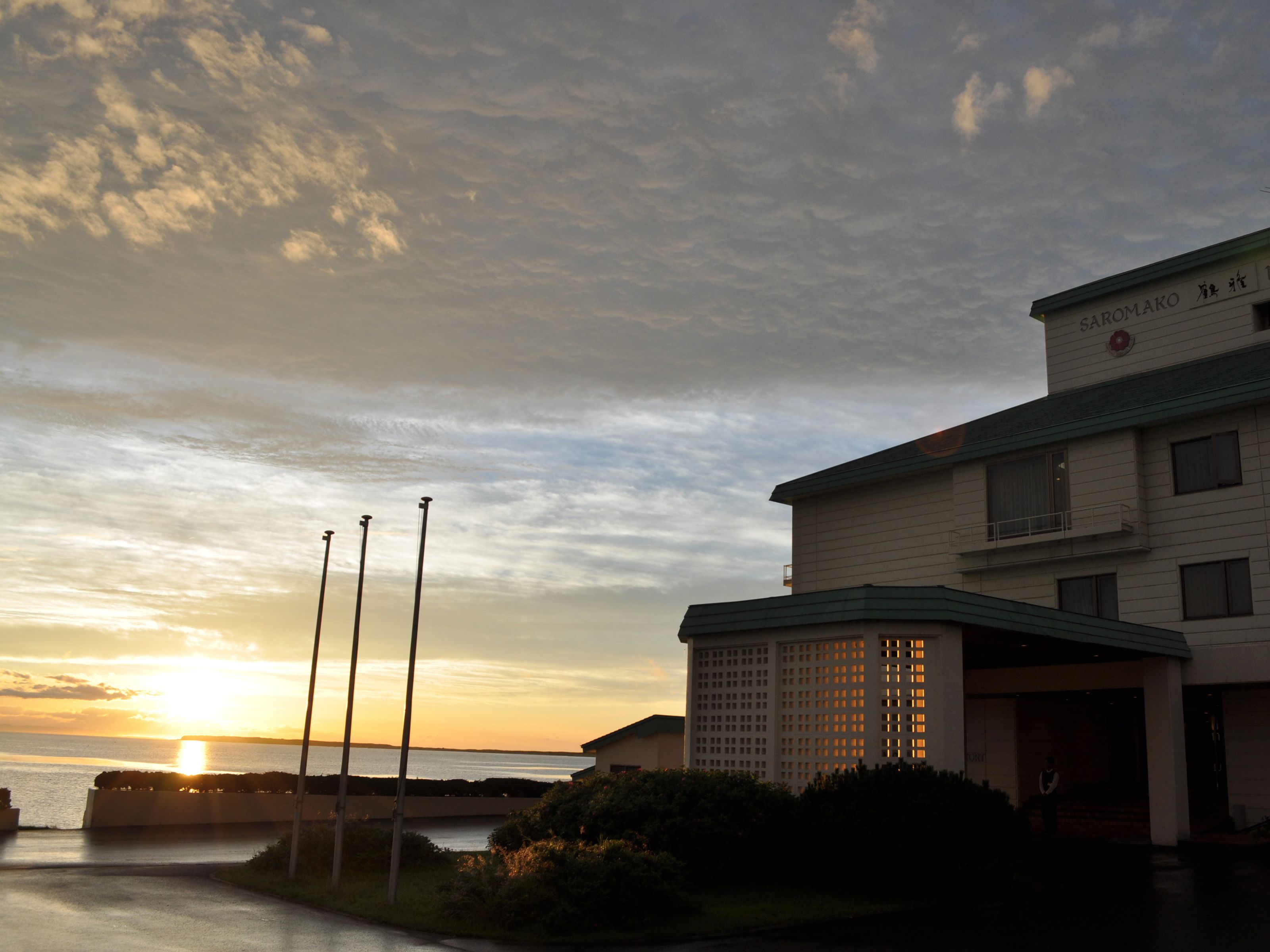 A building with a sign reading "SAROMAKO" and a view of the sunset over water.