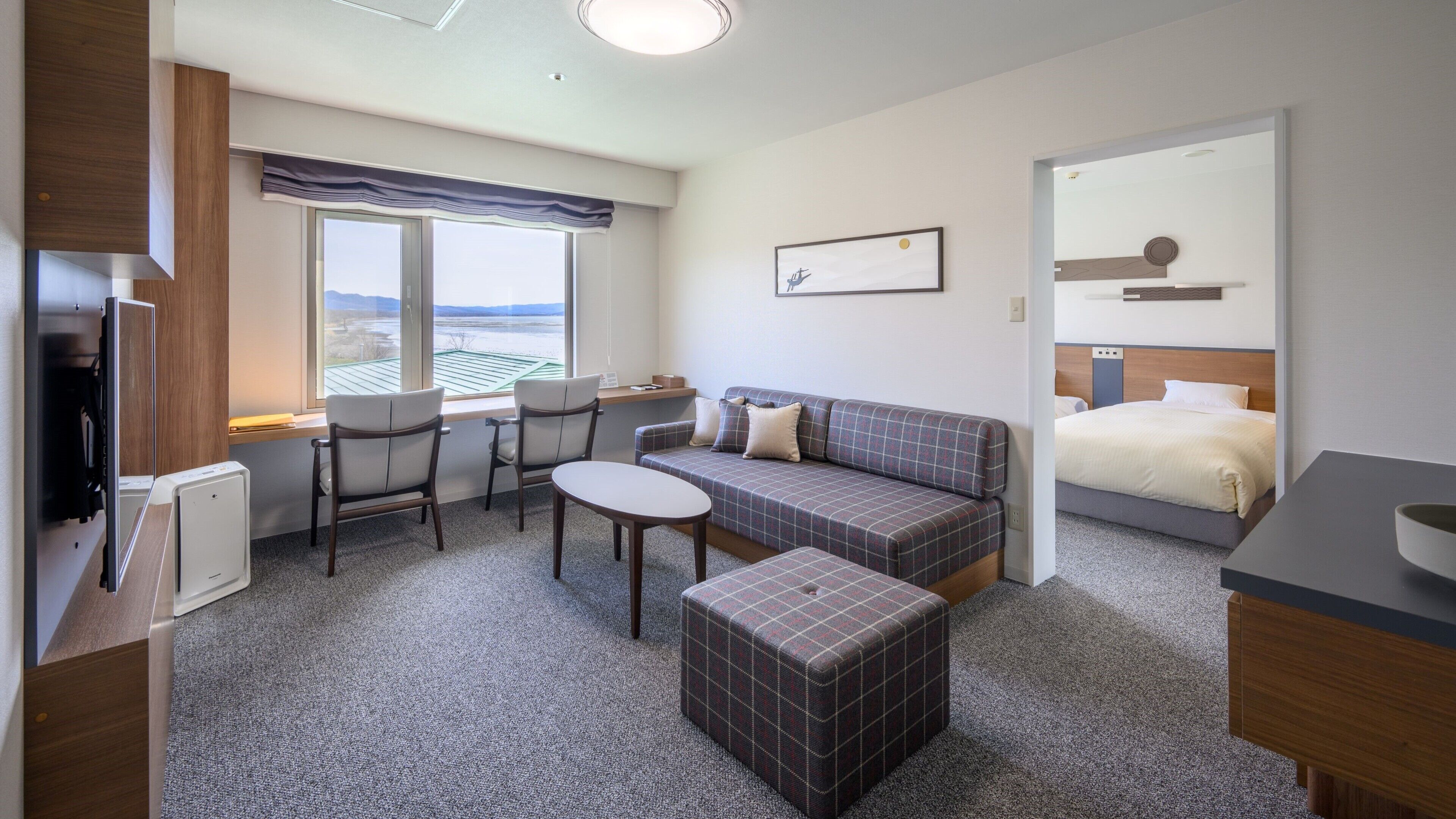 A hotel room with a sofa, two chairs, a small table, a bed, and a window with a view.