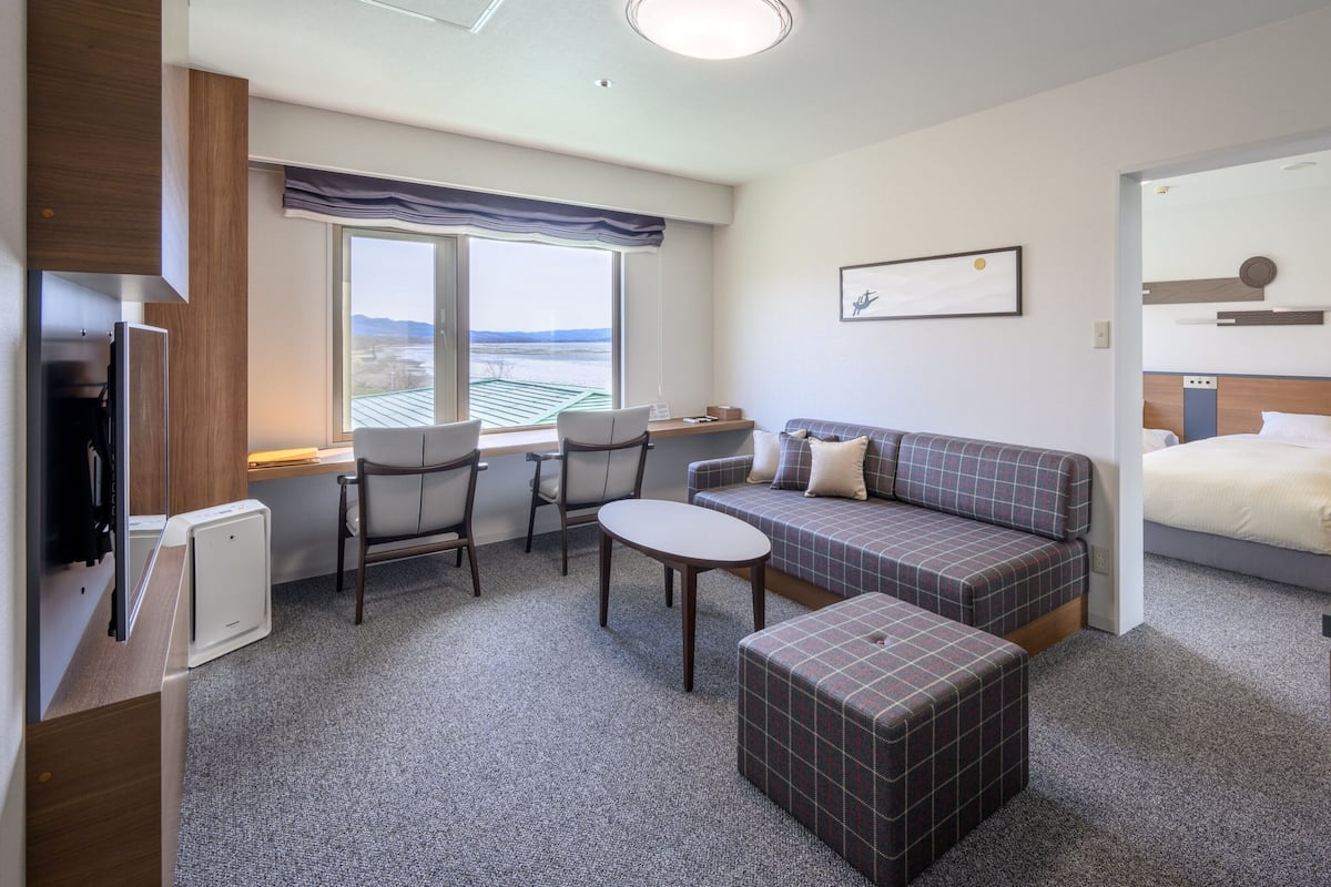 A hotel room with a sofa, two chairs, a small table, a bed, and a window with a view.