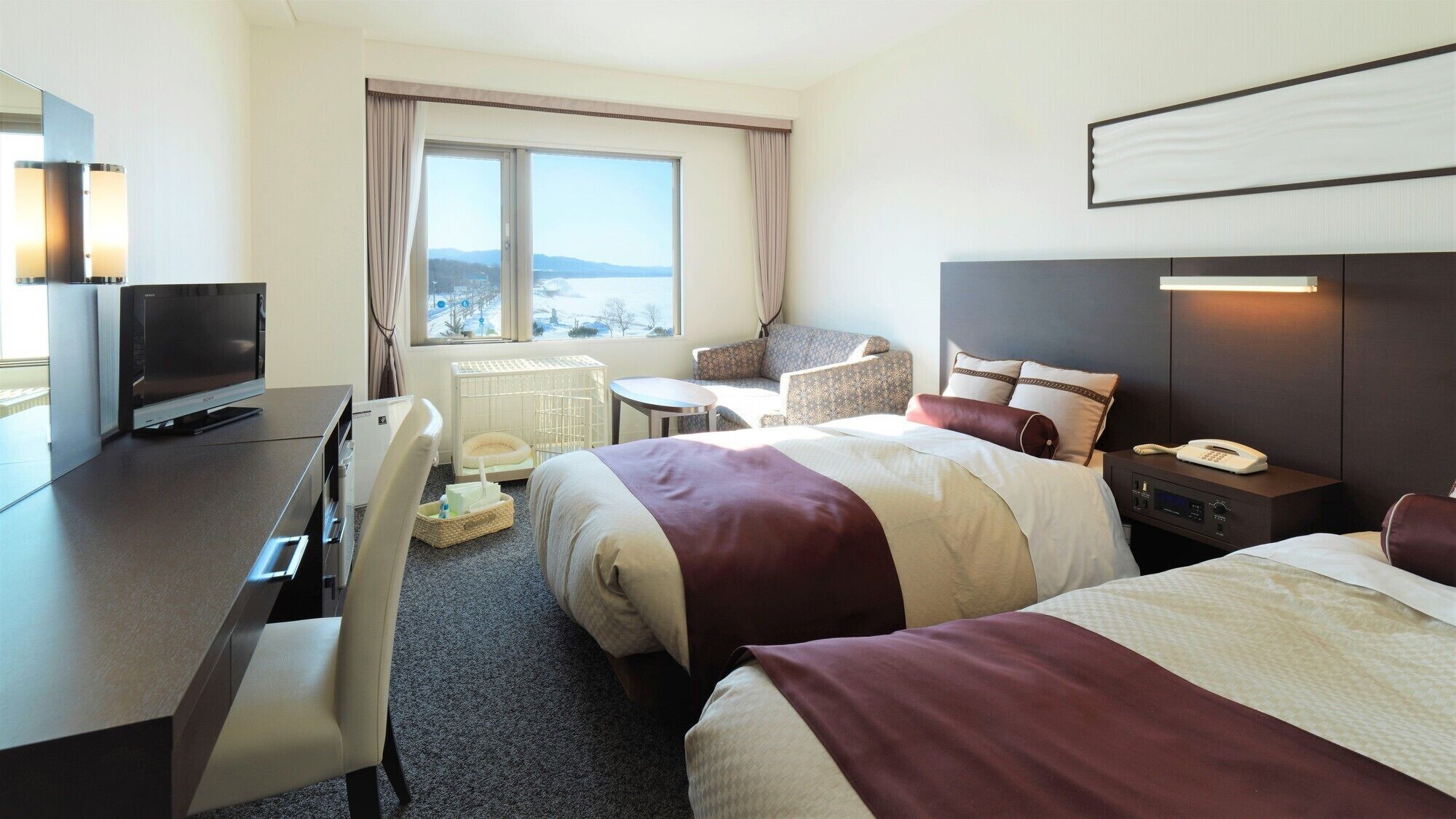 Habitación de hotel con cama, escritorio con televisor, silla, mesita y ventana con vistas.