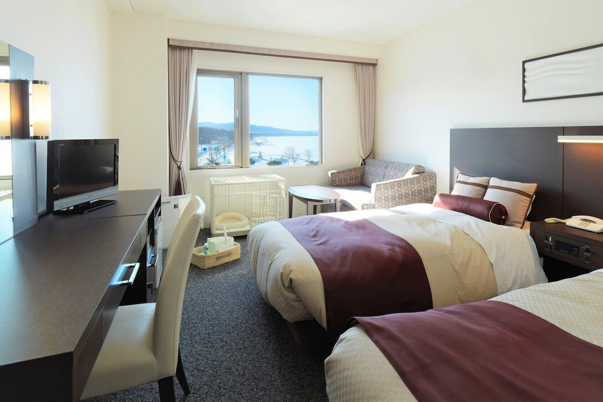 Ein Hotelzimmer mit Bett, Schreibtisch mit Fernseher, Stuhl, einem kleinen Tisch und einem Fenster mit Aussicht.