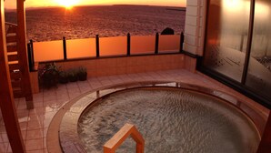 Un jacuzzi con vista al atardecer sobre el océano, rodeado de pisos de cerámica y barandas de madera.