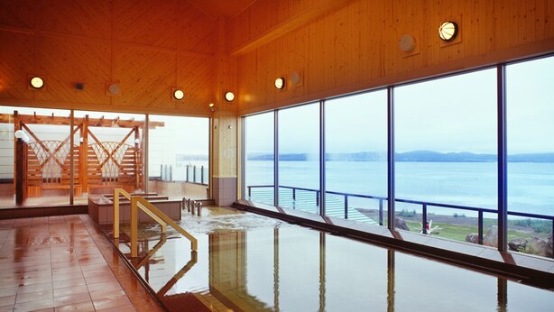 Una amplia piscina interior con vistas al mar, interior de madera y una escalera que lleva a un nivel superior.