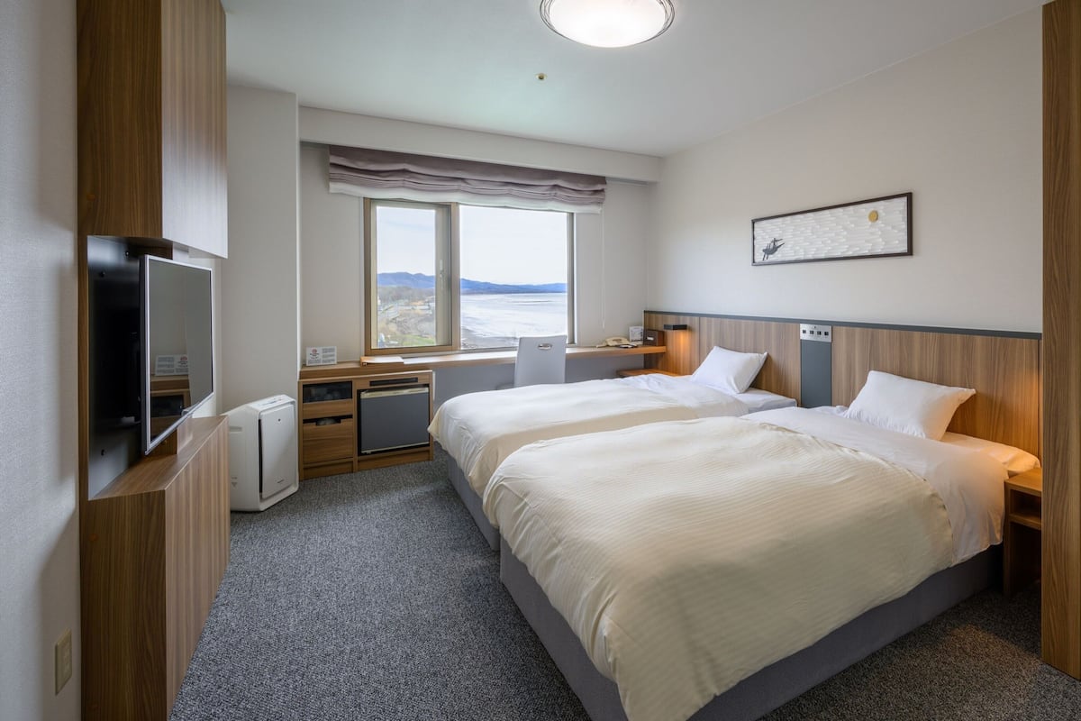 A hotel room with two beds, a desk, a TV, and a window with a view.
