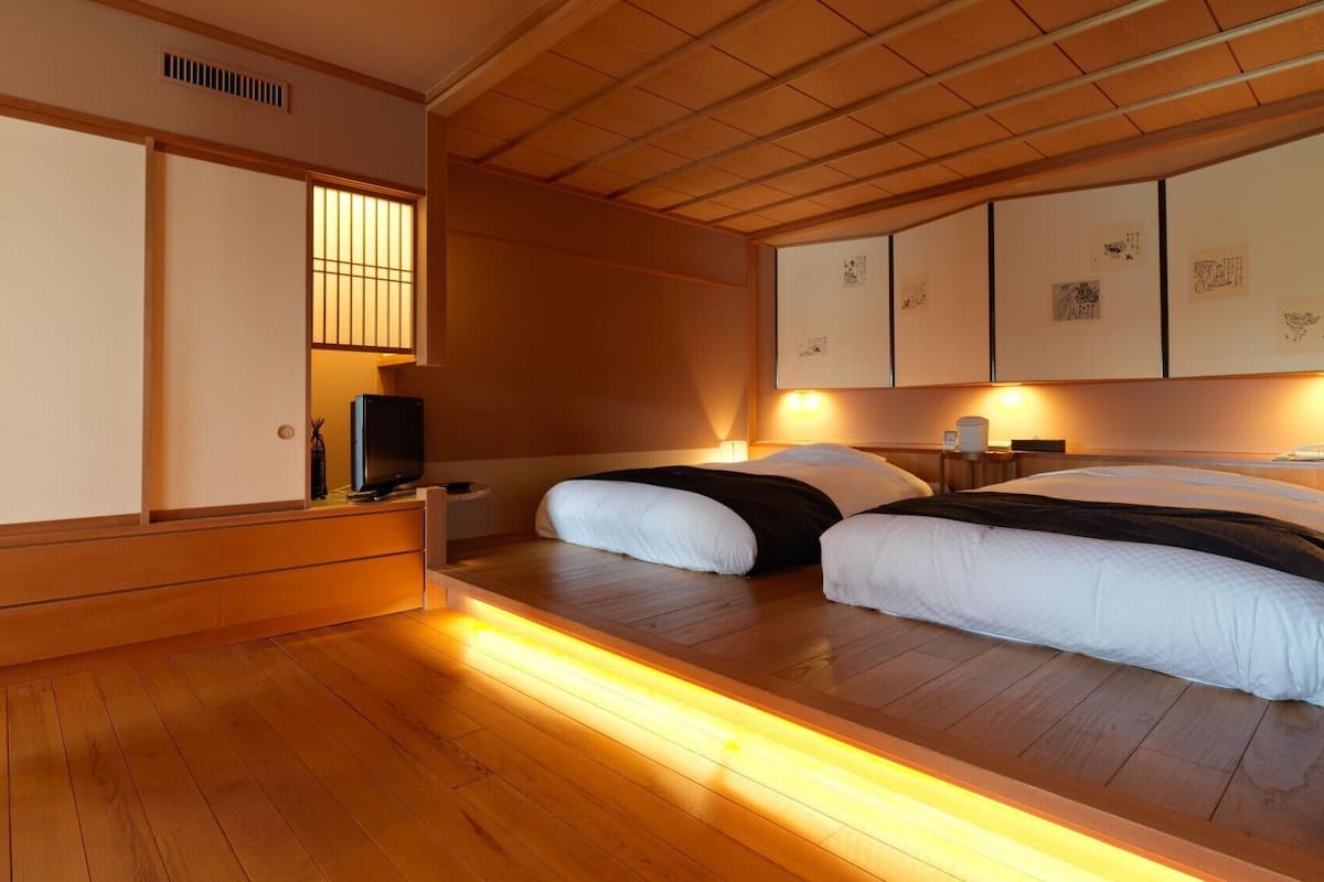 A traditional Japanese-style room with a low platform bed, wooden flooring, sliding doors, and a television.