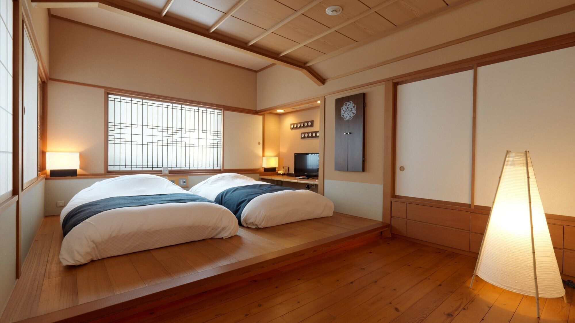 A hotel room with a low wooden platform bed, a TV, a lamp, and a sliding door.