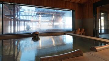 A modern indoor pool with a large window, wooden walls, and a stone seating area.