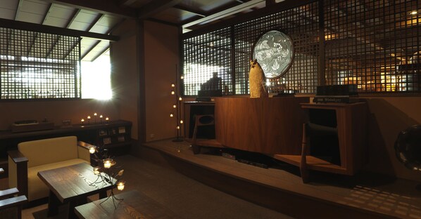 Un interior japonés tradicional con suelo de tatami, una mesa de madera baja, un banco acolchado y un biombo con un ventanal circular.
