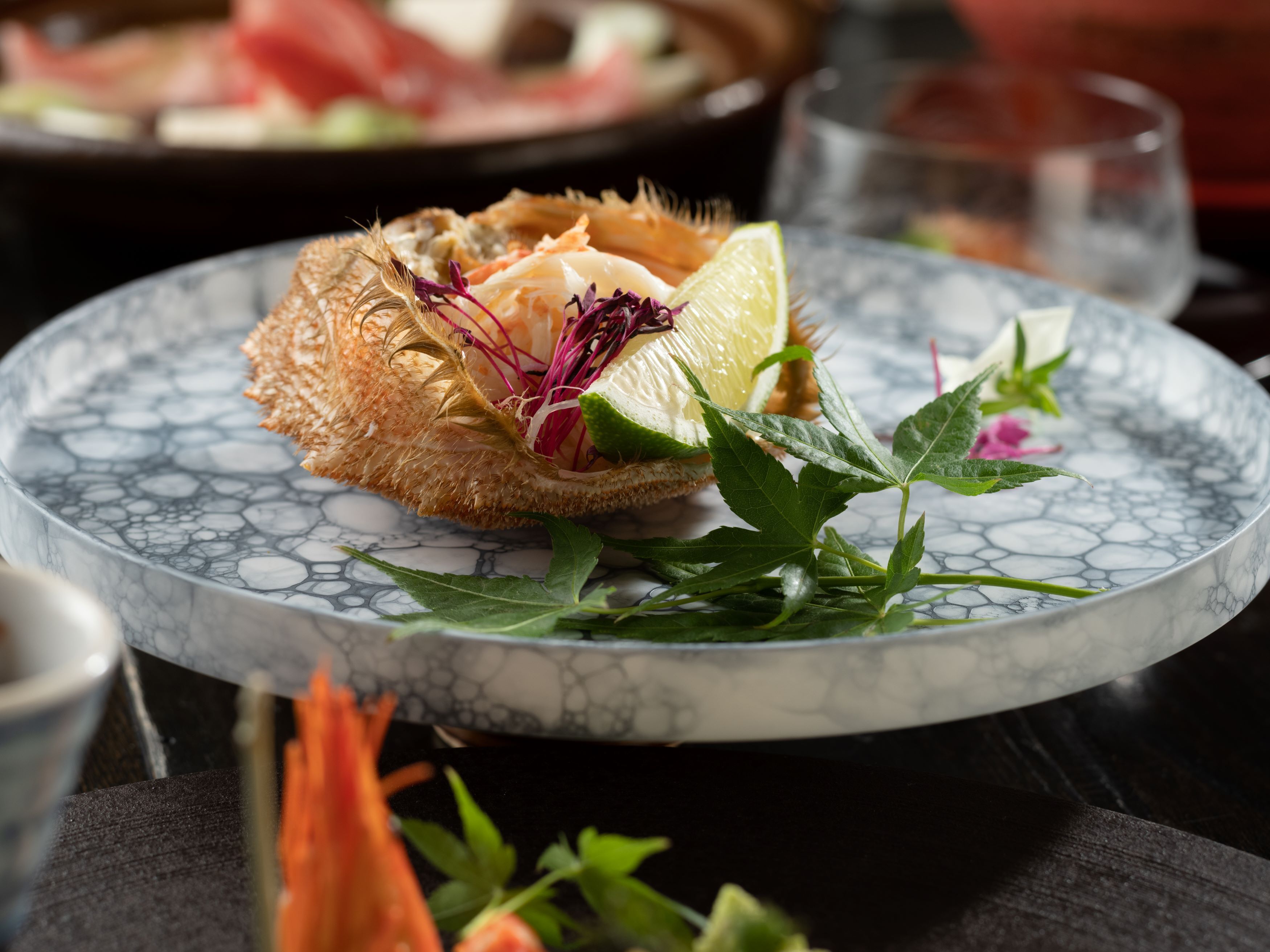 A plate with a seafood dish, garnished with herbs and a slice of lime, on a marble table.