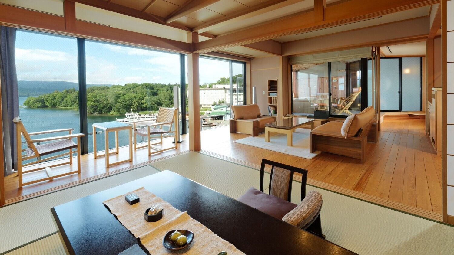 A spacious living area with a large window overlooking a lake, a dining table with tatami mats, and a cozy seating area with cushions.