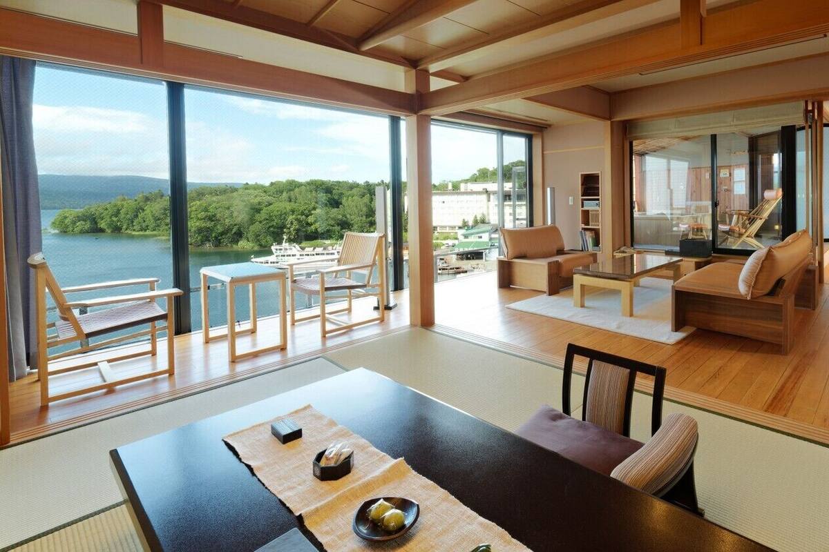 A spacious living area with a large window overlooking a lake, a dining table with tatami mats, and a cozy seating area with cushions.