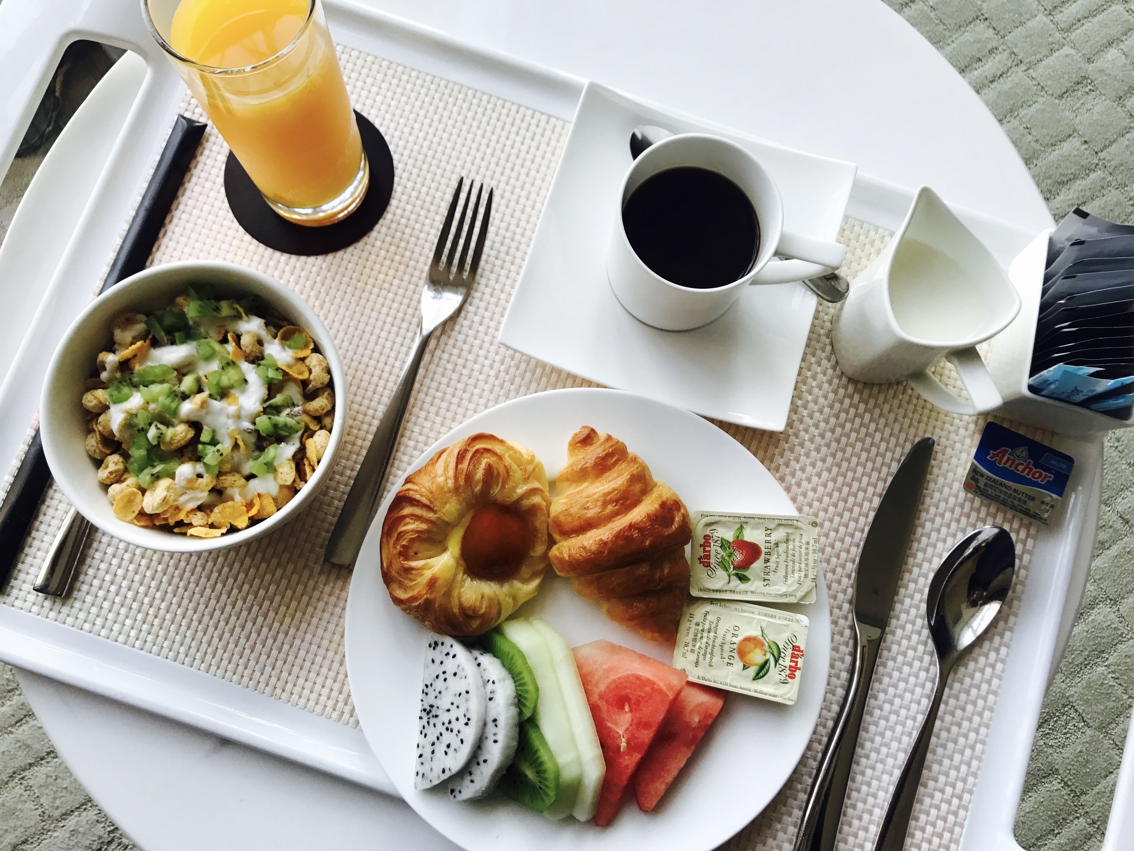 Bandeja de desayuno con cruasanes, un tazón de cereal, fruta fresca y un vaso de jugo de naranja.