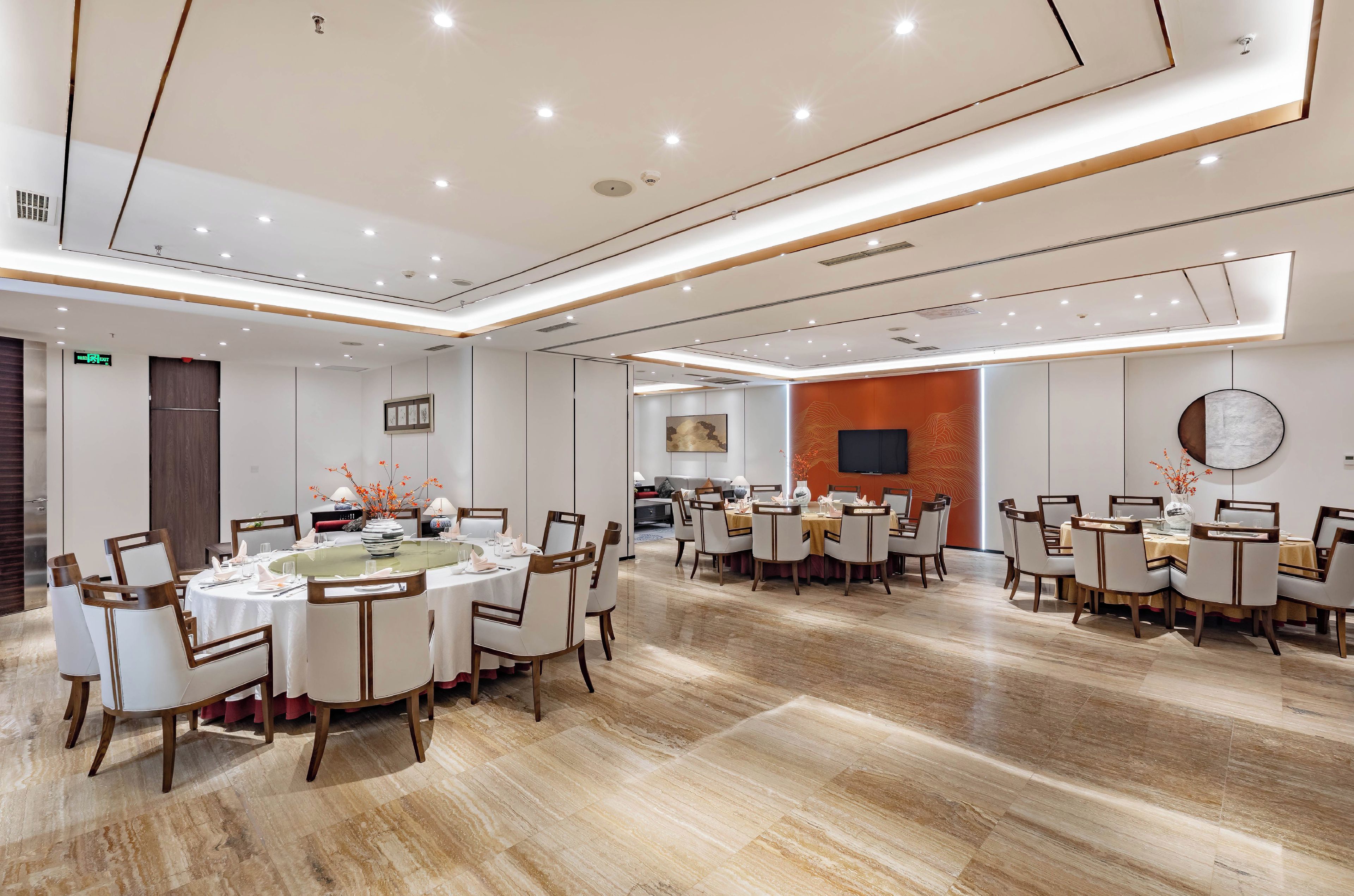 A spacious dining area with multiple round tables, chairs, and a modern ceiling design.