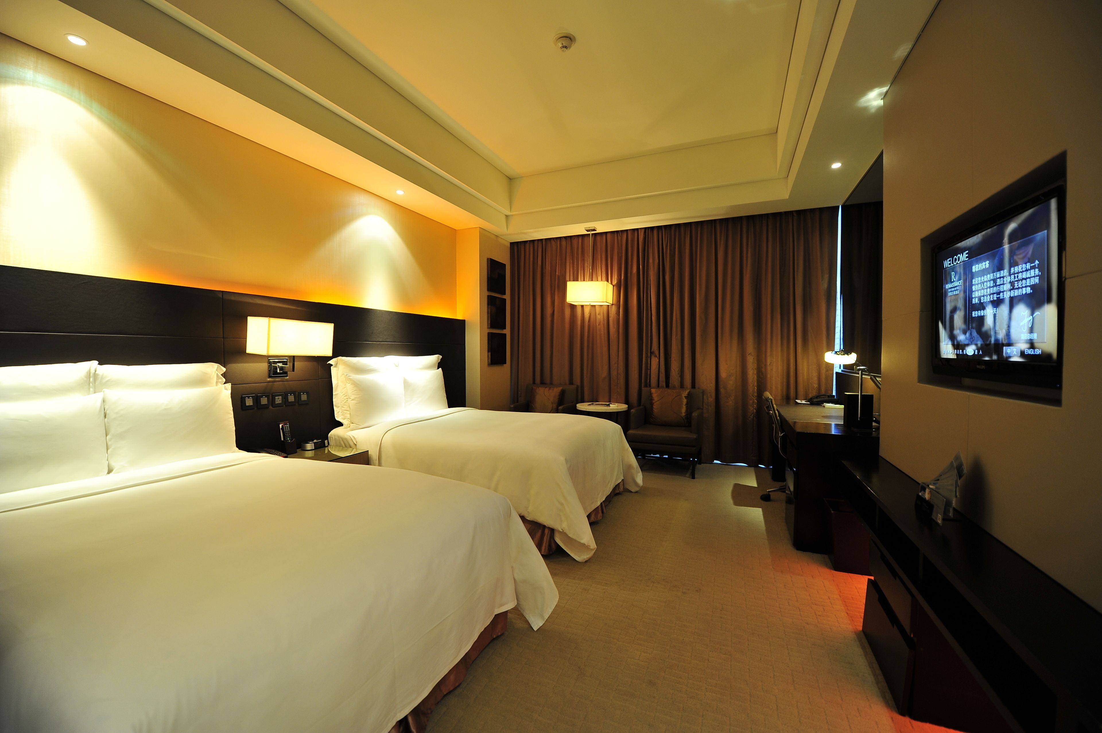 A hotel room with two beds, a desk, a TV, and a seating area.