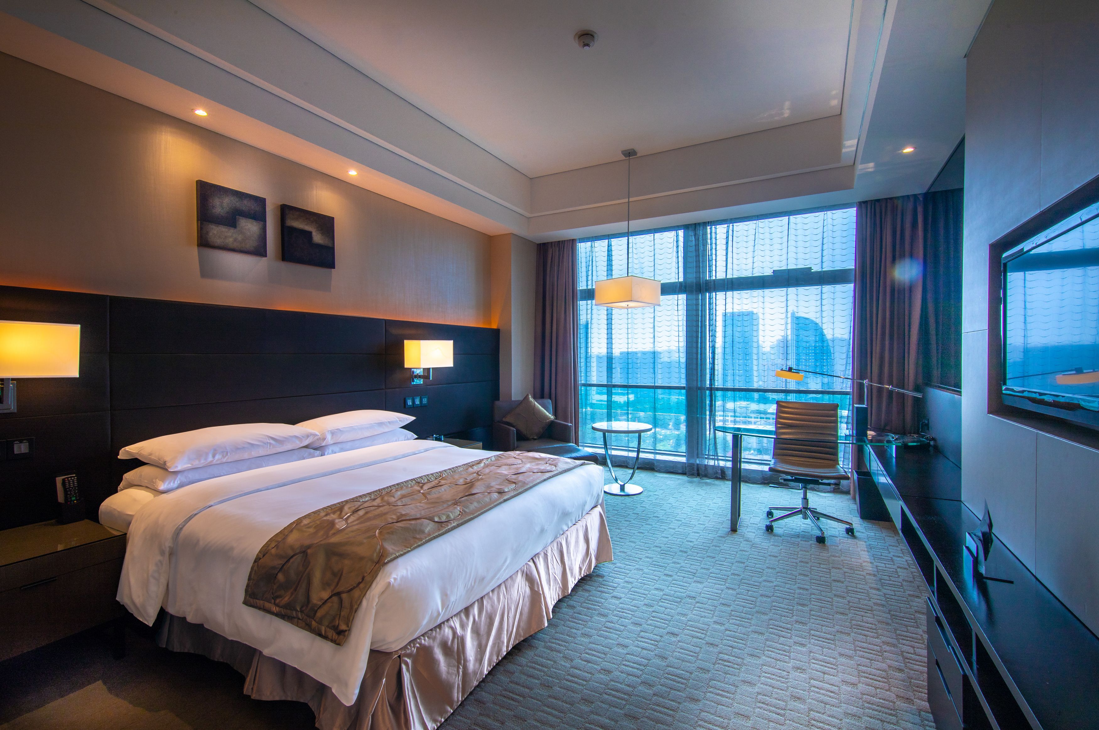 A hotel room with a large bed, a desk, a chair, and a TV.